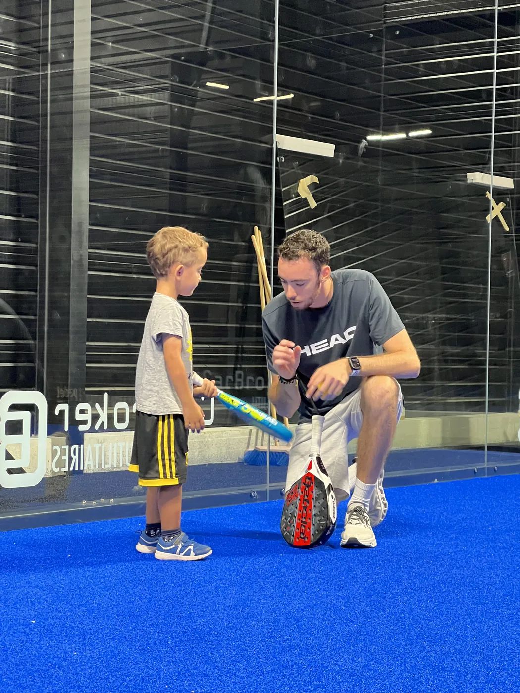 Un coach de Two Padel, accroupi à hauteur d'un jeune joueur, lui montre comment tenir sa raquette sur la piste bleue